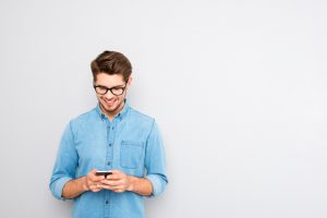 Happy man in glasses typing sms on gray background